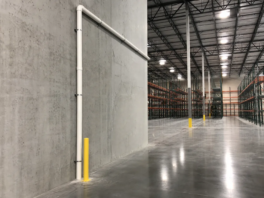 Radon mitigation piping routed along the wall of a Los Angeles warehouse above forklift traffic
